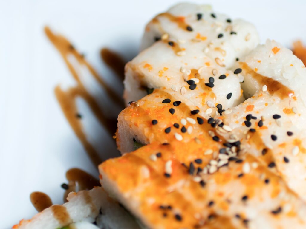 Vibrant close-up of sushi rolls garnished with sesame seeds and drizzled soy sauce.