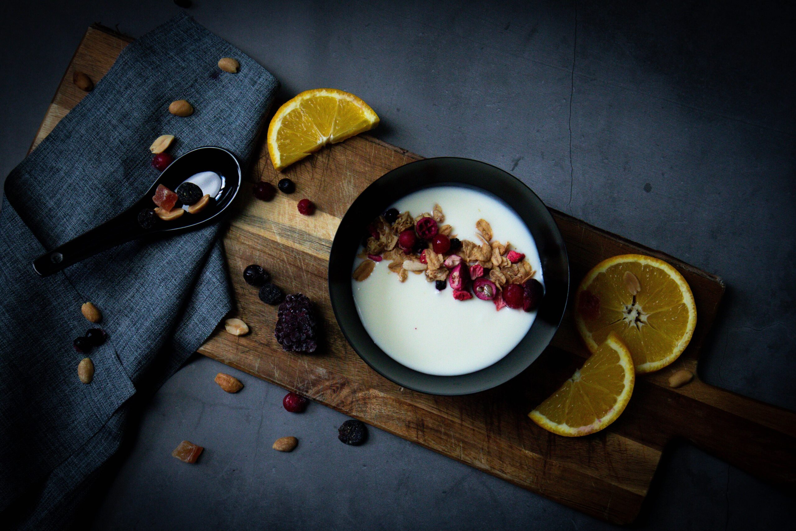 Top view of a breakfast bowl with yogurt, fresh fruits, and granola on a wooden board.